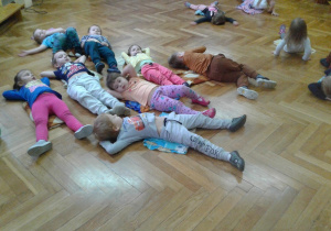 Dzieci z grupy młodszej leżą na podłodze, odpoczywając po zawodach